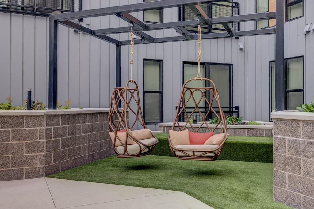 Two hanging chairs are suspended from a metal frame in a backyard.
