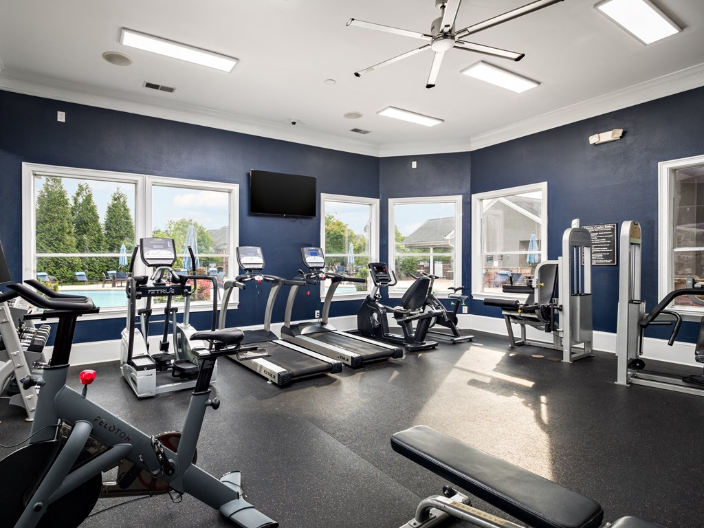 a gym with cardio equipment and windows with a view of a pool