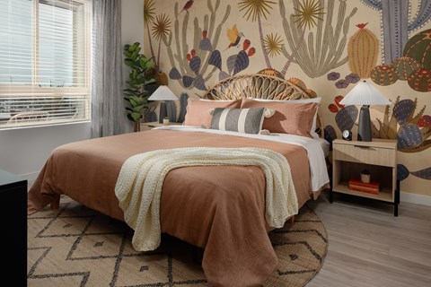 A bedroom with a bed covered in a peach blanket and a cactus wallpaper.