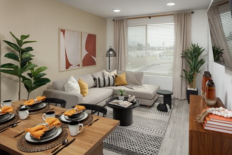A dining table set with plates and napkins is in the foreground of a living room with a grey couch and a coffee table.