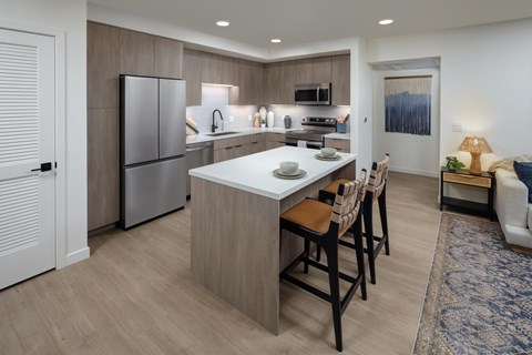 A modern kitchen with a white island and wooden chairs.