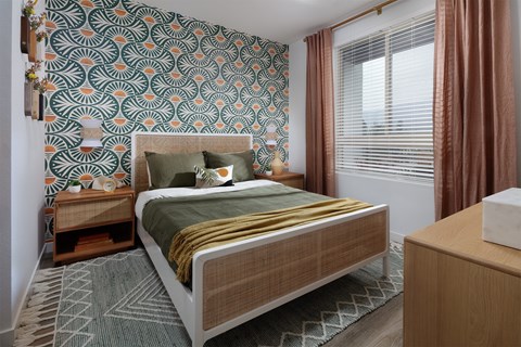 A bedroom with a patterned wallpaper and a bed with a green blanket.