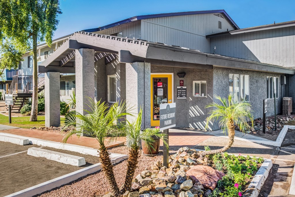 a building with a yellow door and a porch with palm trees in front of it