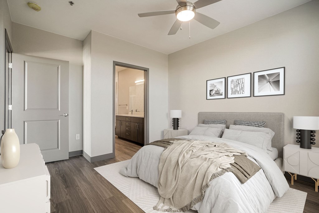 Virtually staged bedroom with view into bathroom and wood style flooring  at Novus, Lone Tree, 80124