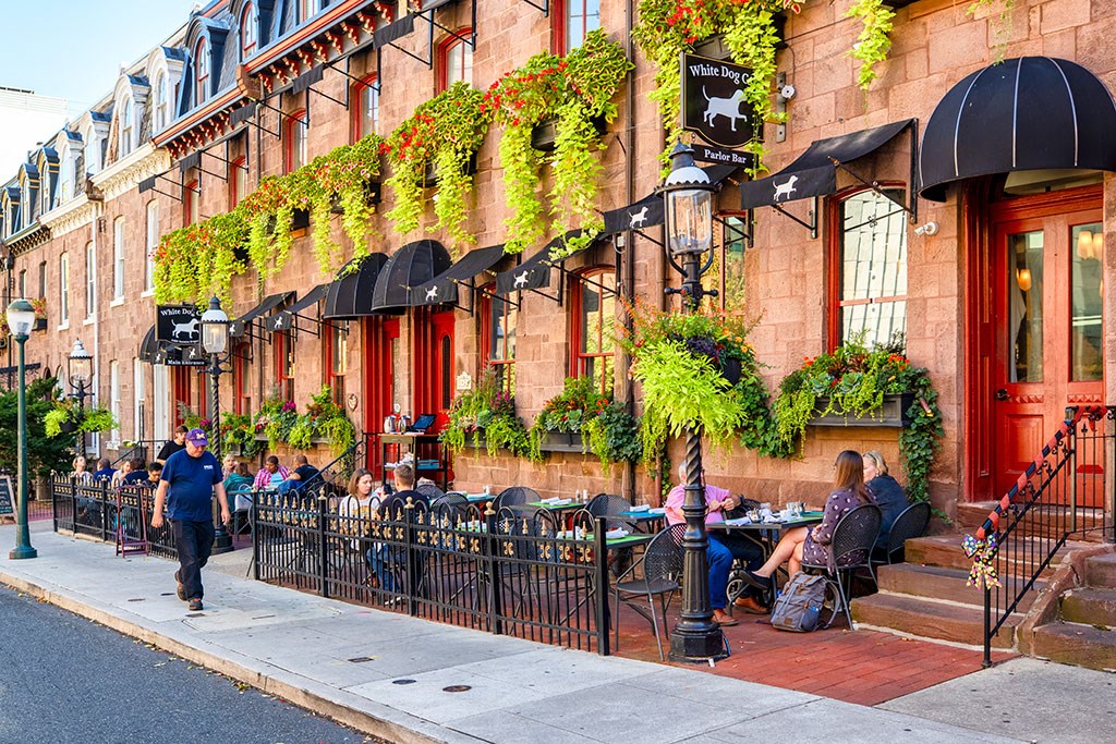 people sitting at tables outside of a restaurant on a city street