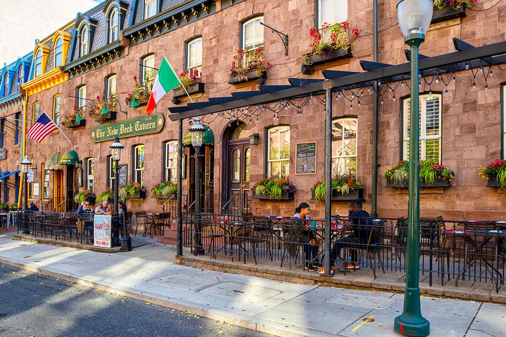 people sitting at tables outside of a restaurant on a city street