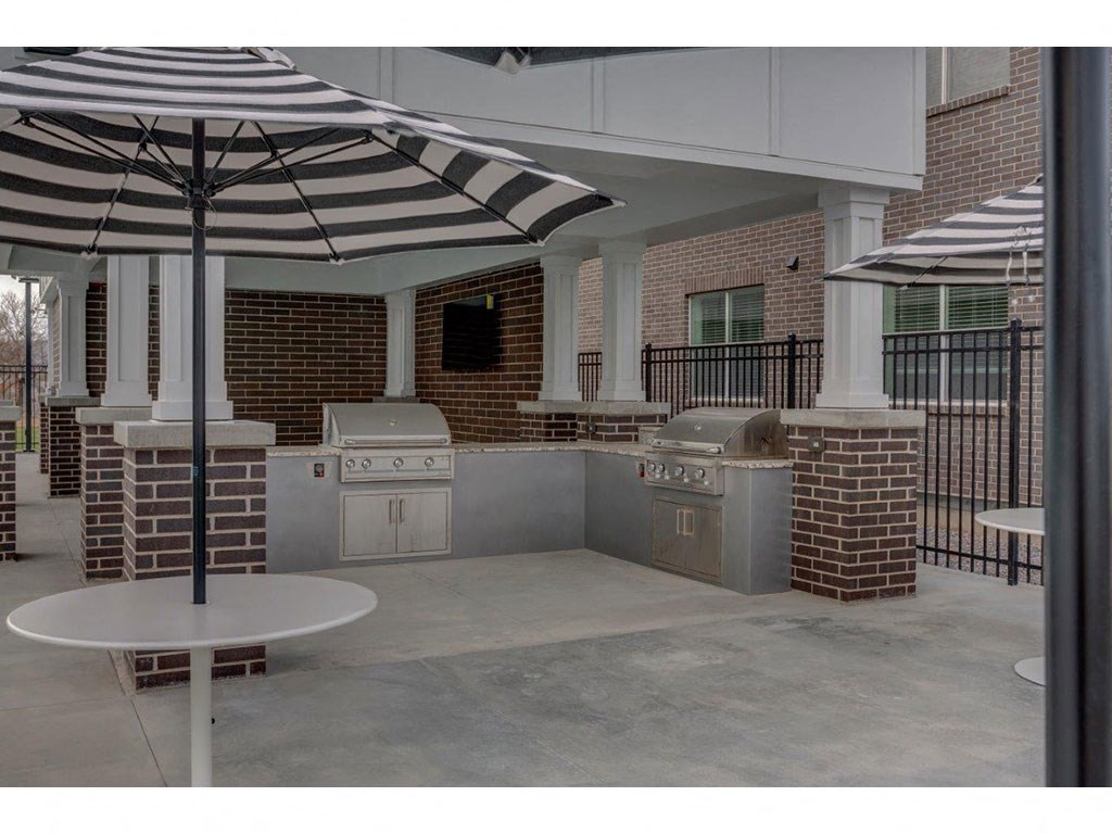 a patio with an outdoor grill and tables with umbrellas