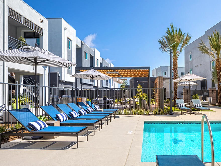 a pool with blue lounge chairs and umbrellas near a building