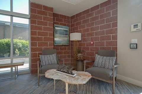 a living room with two chairs and a table in front of a brick wall