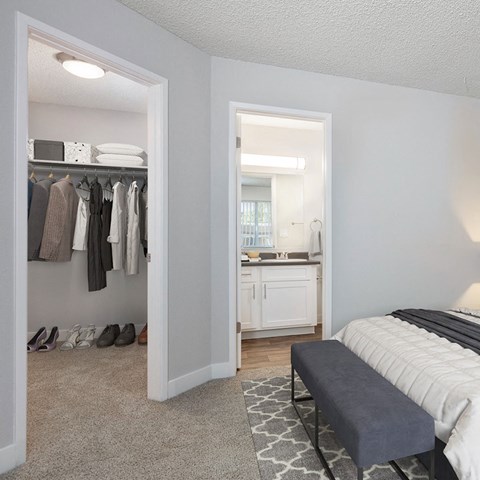 A bedroom with a view into the entry of the bathroom and a view of a spacious closet with well organized clothing and shoes.