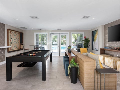 A black pool table is in the middle of a living room with a couch and a television.