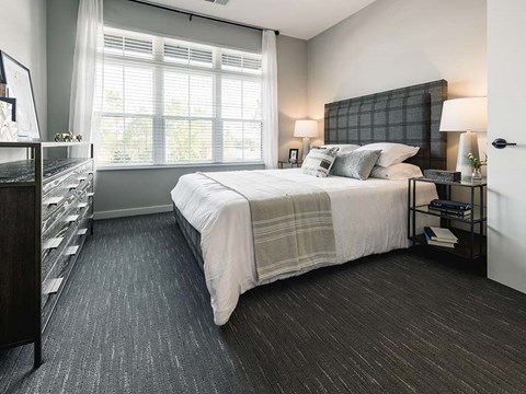 A bedroom with a large bed and a window with white curtains.