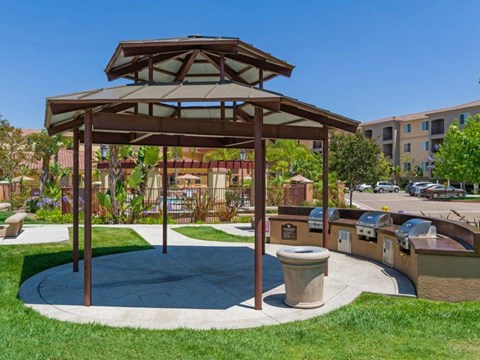 A gazebo is surrounded by a grassy area and a concrete walkway.