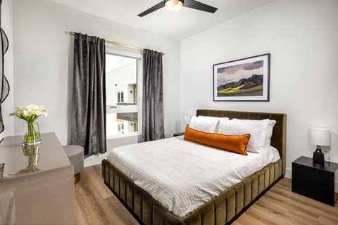 A bedroom with a large bed, a ceiling fan, and a painting on the wall.