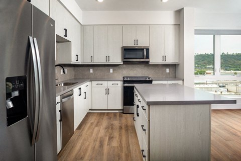 A modern kitchen with a refrigerator on the left and a microwave above the stove.