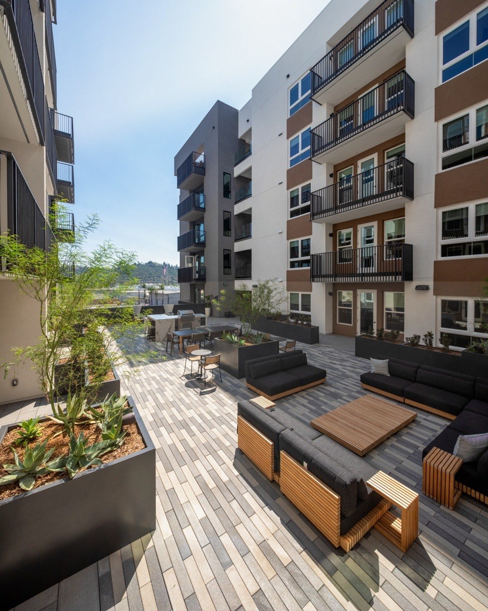 A modern outdoor seating area with black couches and wooden tables.