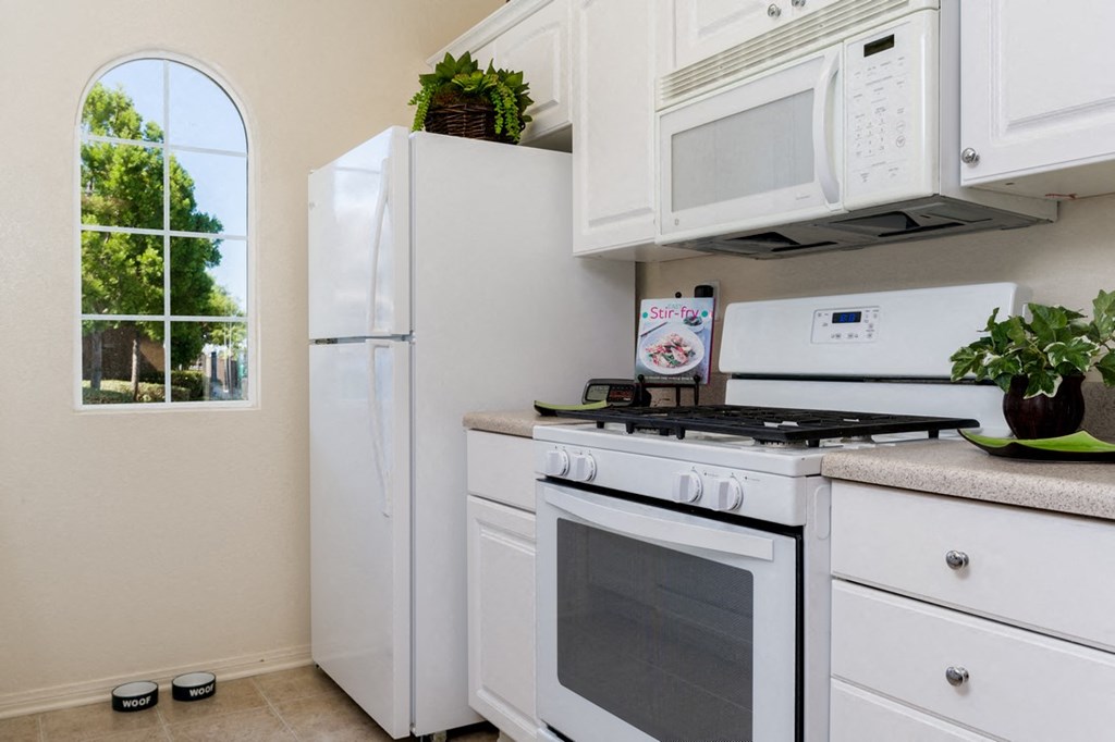 A white kitchen with a stove, refrigerator, and microwave.