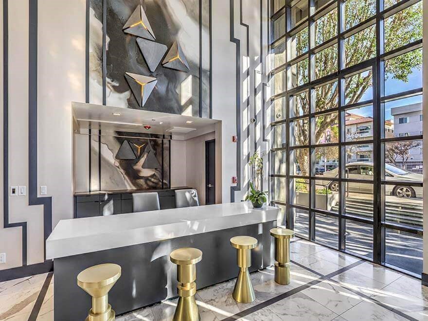 a bar with gold stools in a lobby with large windows