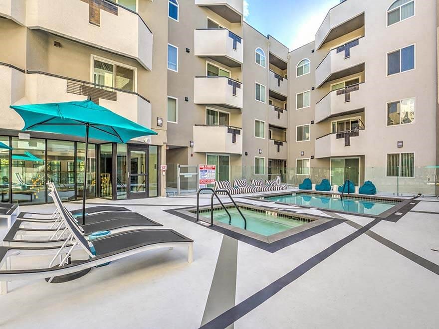 a pool with lounge chairs and umbrellas in front of an apartment building