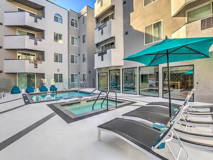 a pool with chairs and umbrellas in front of an apartment building