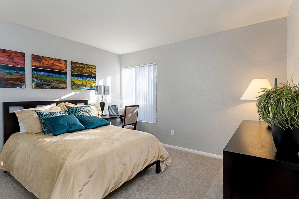 A bedroom with a bed, nightstand, lamp, and a plant. A bedroom with a bed, nightstand, lamp, and a plant at The Casas Apartments, San Diego, CA