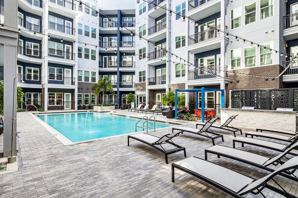 an outdoor swimming pool with chaise lounge chairs in front of an apartment building