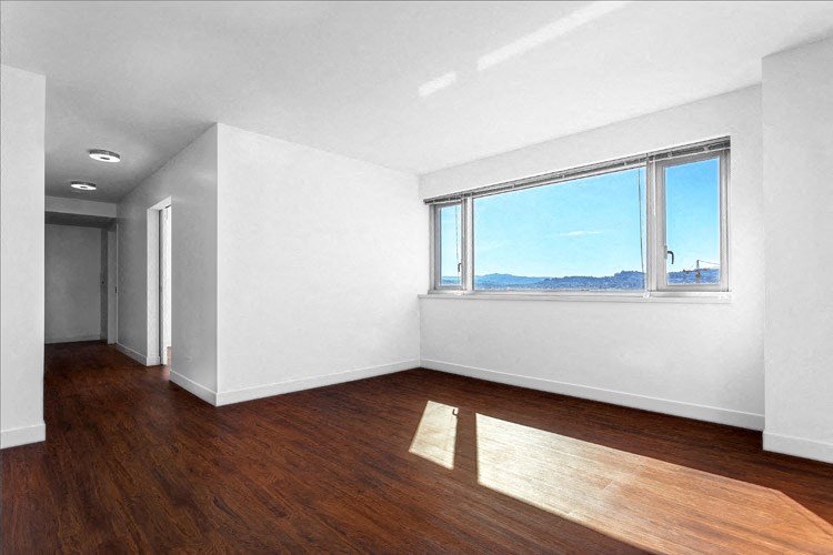 2-BR Apartments in San Francisco, CA - Trinity Place at 1190 - Living Room with Wood-Style Flooring, a Large Window, and a Hallway to Other Rooms