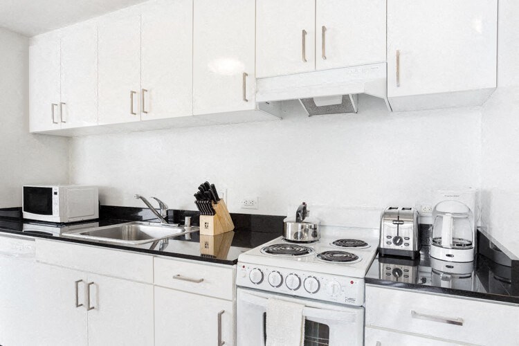SOMA Apartments - Kitchen With Black Granite Counters, White Cabinets, Sink, Electric Stove Top, And Oven.