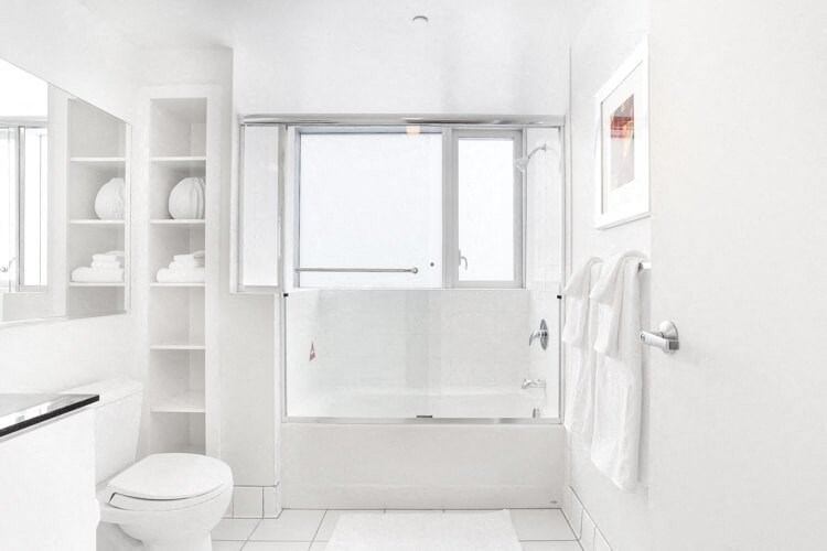 San Francisco Luxury Apartments - Large Bathroom With Black Granite Counters, Vanity Mirror, Toilet, Window, Shower With Tub, Ceramic Tile Flooring, And Wall Shelves.