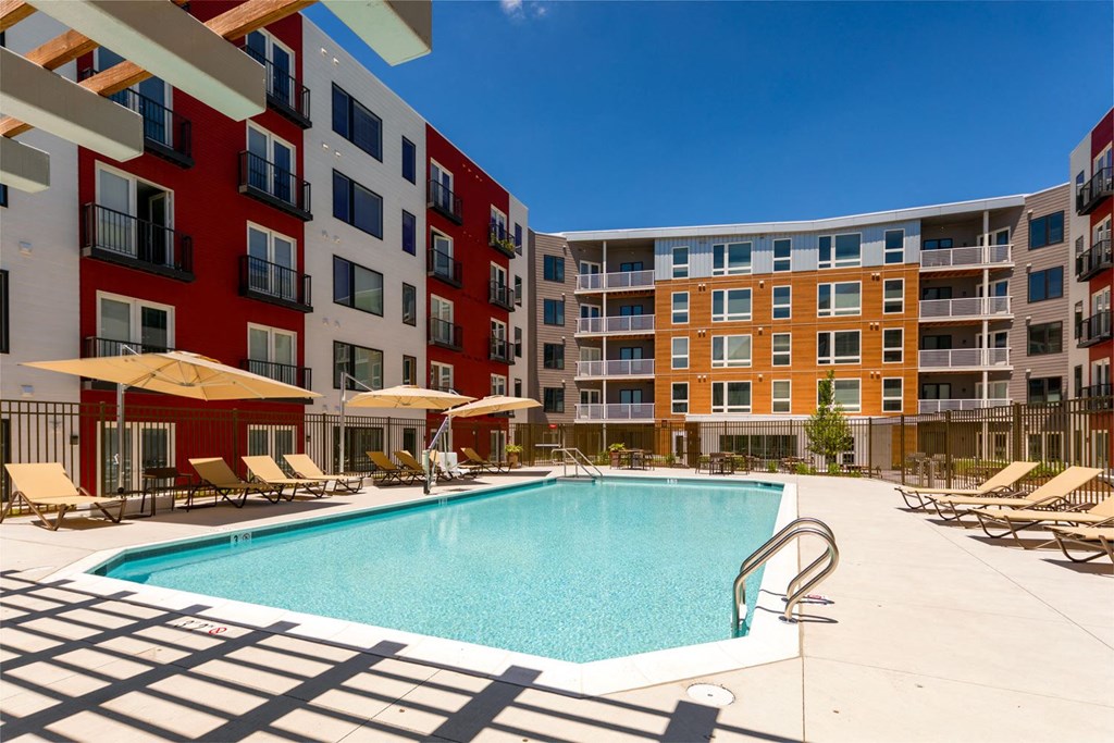 a swimming pool with chaise lounge chairs and umbrellas in front of an apartment building