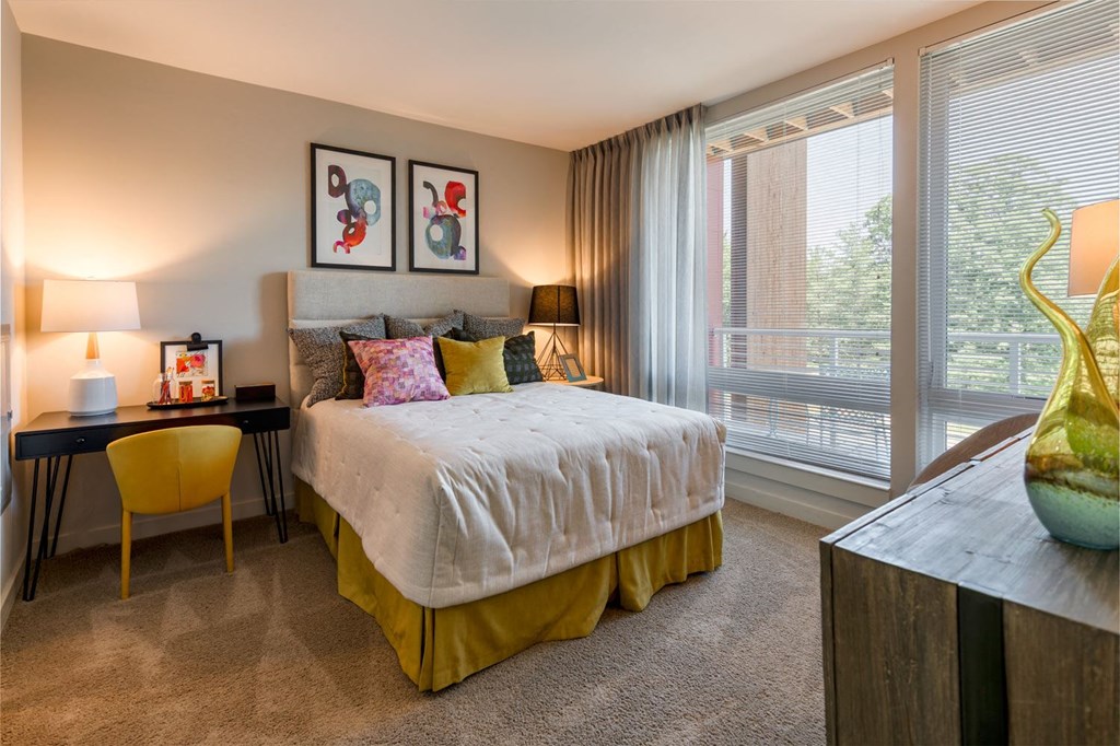 a bedroom with a large window and a large bed with a white comforter