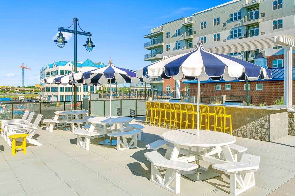 an outdoor patio with white tables and yellow chairs and a large building in the background