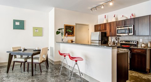 A kitchen with a table and chairs in the foreground and a counter with a microwave and oven in the background.