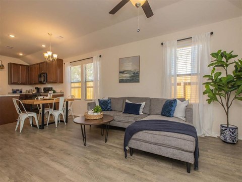 A living room with a grey couch and a dining table with white chairs.