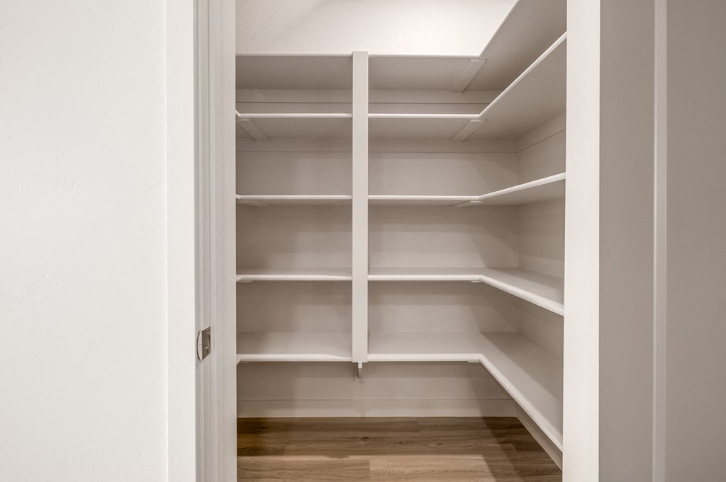 a walk in closet with white shelves and a wood floor