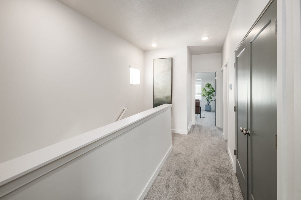a long hallway with white walls and grey carpeting and a door to a hallway