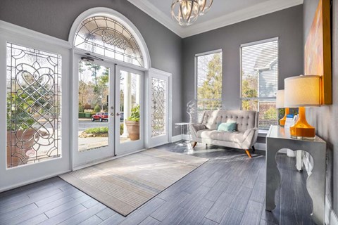 A living room with a grey couch and a large window with a view of a street.