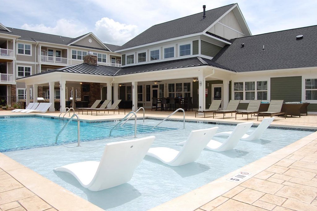 a large swimming pool with white chairs in front of a building