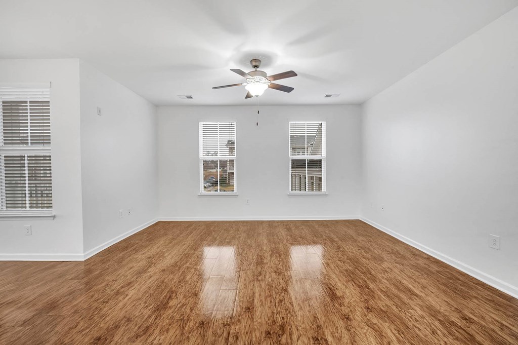 an empty living room with a ceiling fan and windows