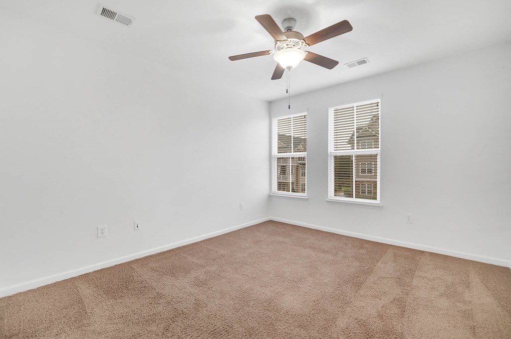 an empty living room with a ceiling fan and two windows