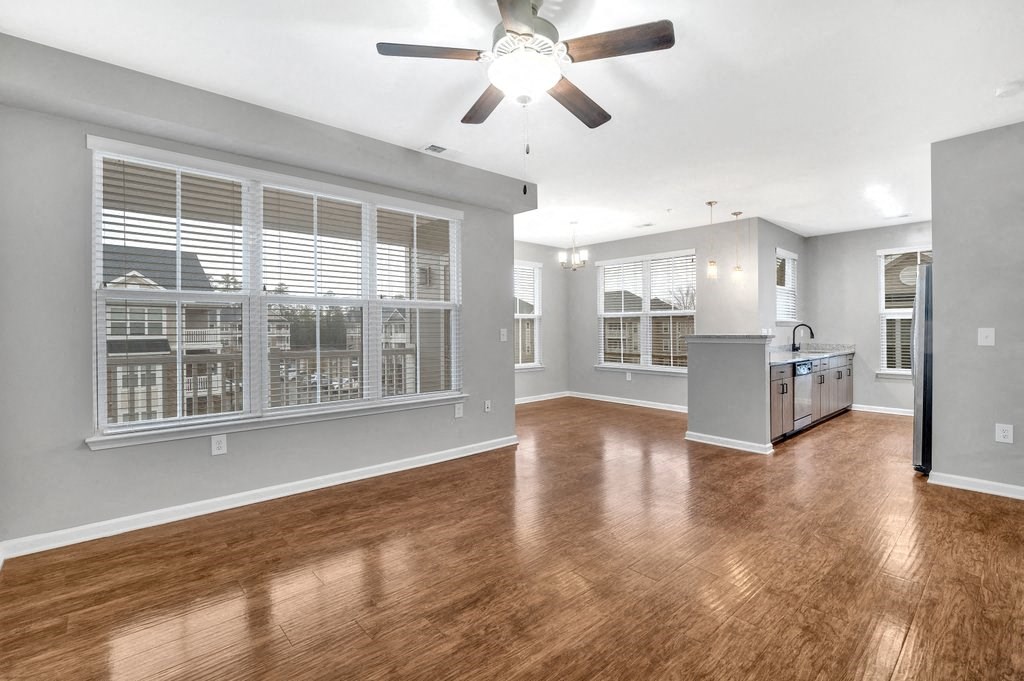 an empty living room with a ceiling fan and a kitchen