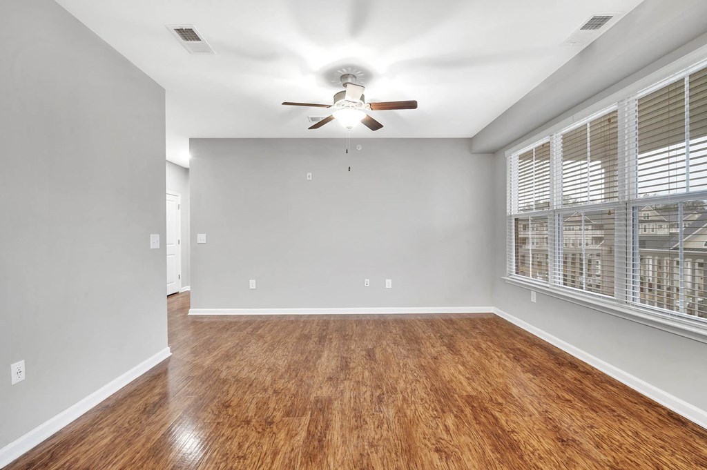 an empty living room with a large window and a ceiling fan