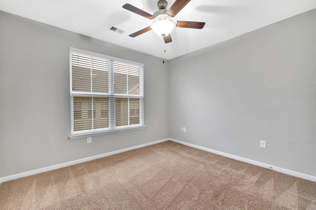 an empty living room with a large window and a ceiling fan