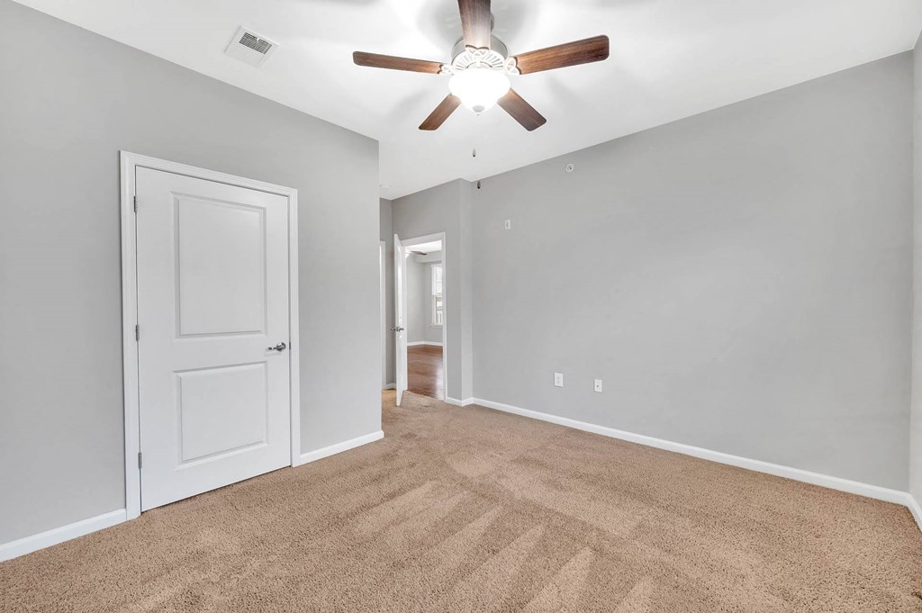 an empty living room with a ceiling fan and a door to a hallway