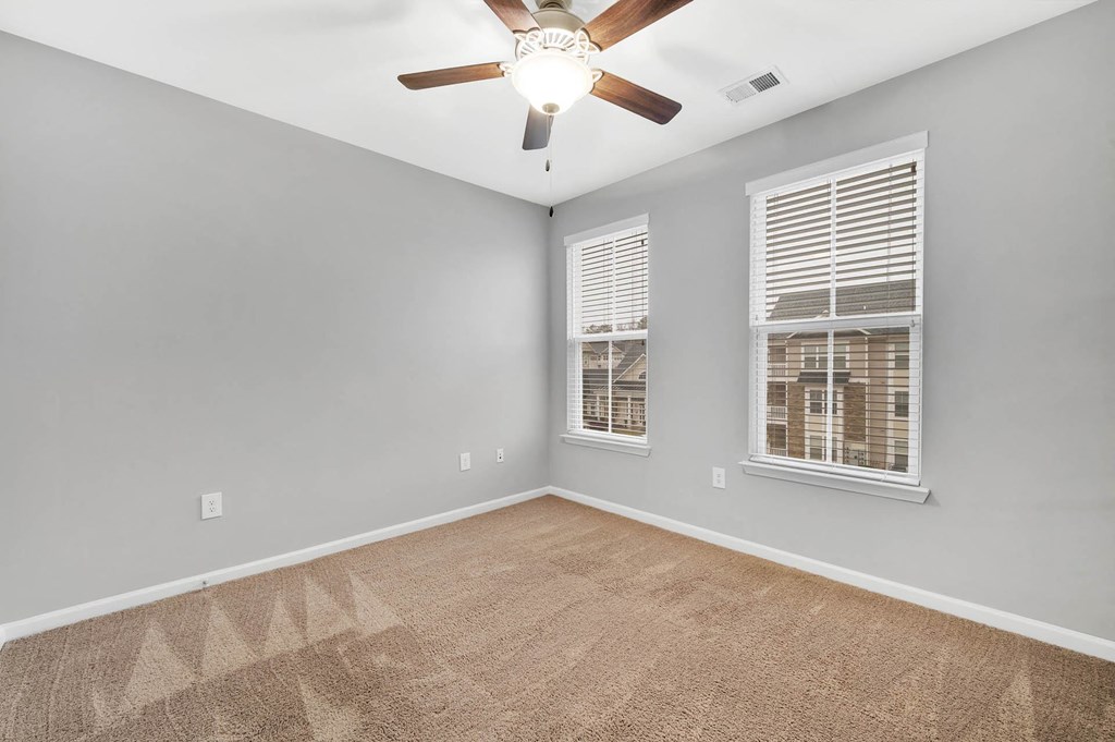 an empty living room with a ceiling fan and two windows