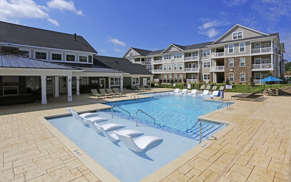 a swimming pool with chairs in front of an apartment building