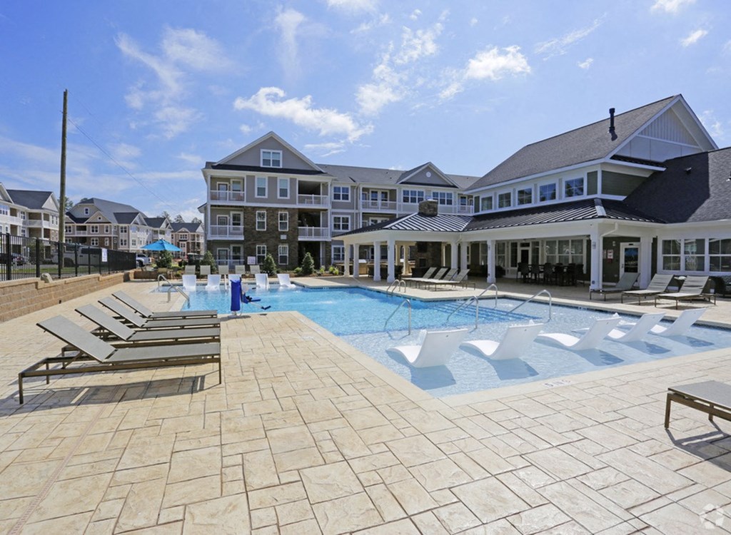 a large swimming pool with lounge chairs and a building in the background
