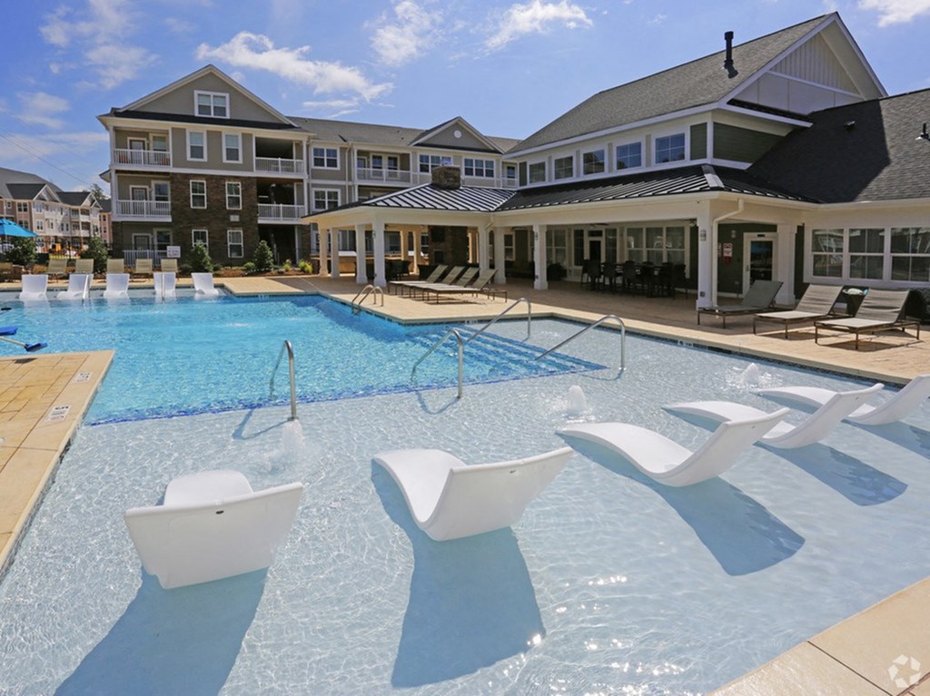 a large swimming pool with white chairs in front of an apartment building