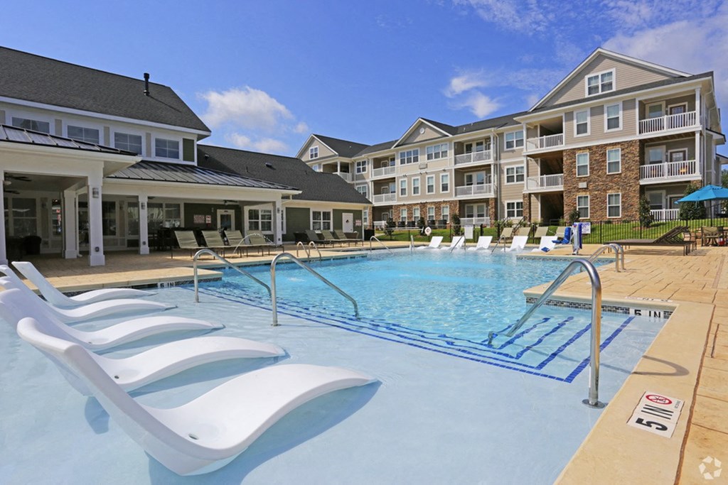 a swimming pool with white chairs in front of an apartment building
