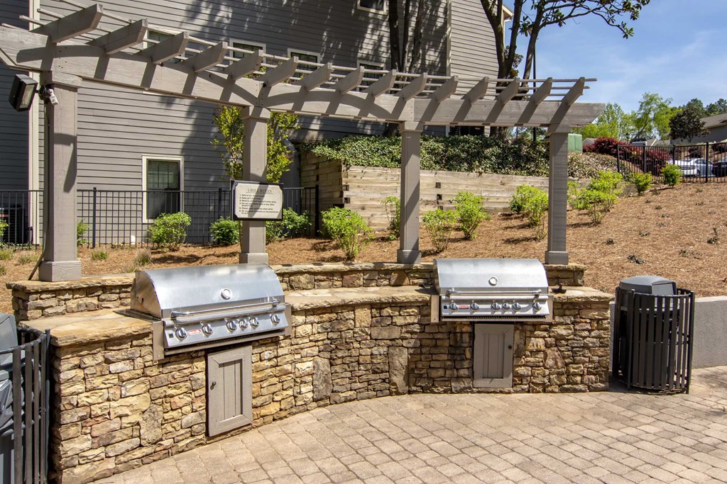 two bbq grills in a backyard with a pergola